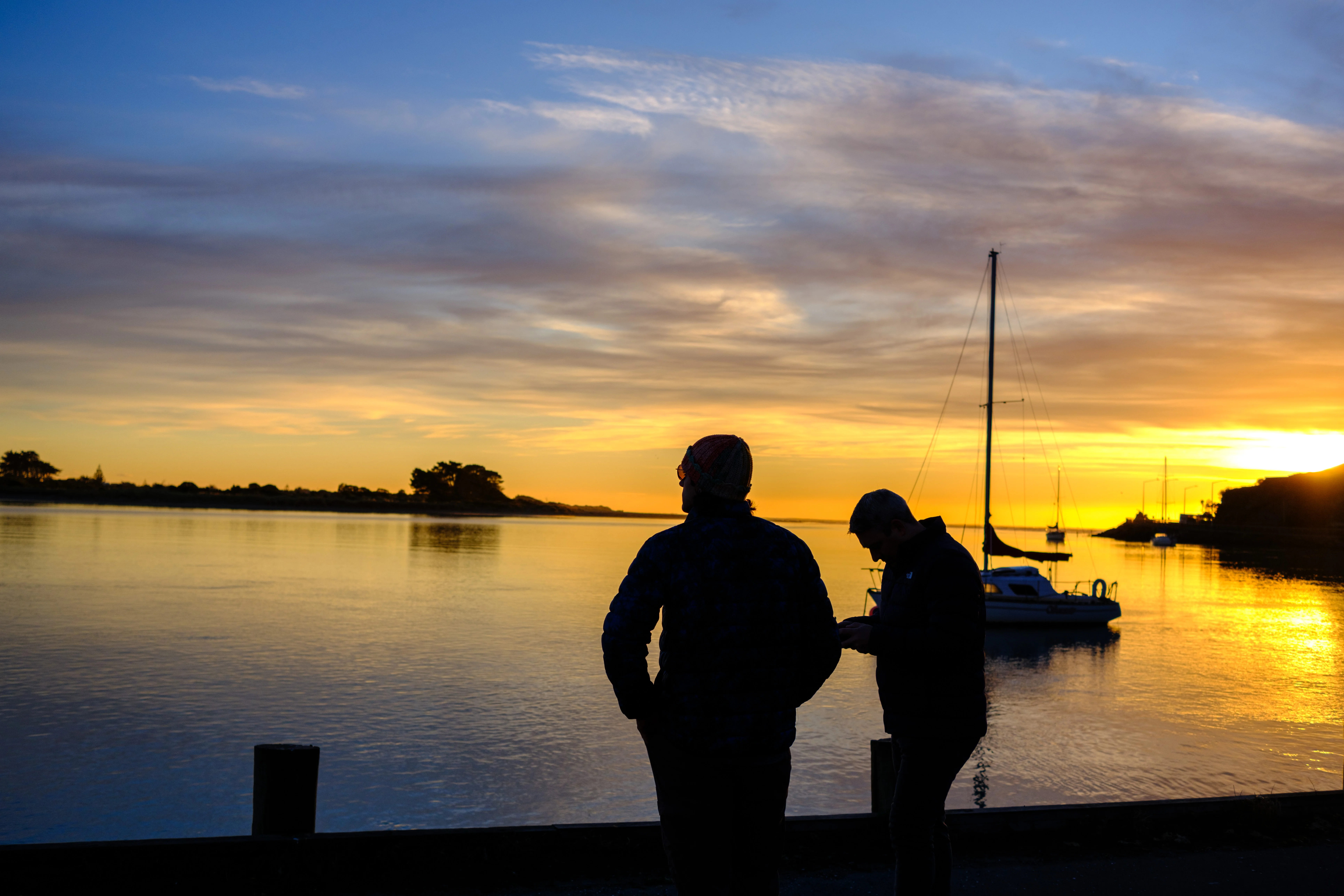 27mm · f/3.6 · 1/1250s · ISO 200
FUJIFILM X-T5 · XF27mmF2.8 R WR · May 24, 2024
Two silhouetted people watch a golden Christchurch sunrise by water.
Christchurch, New Zealand
© Brandon Cook