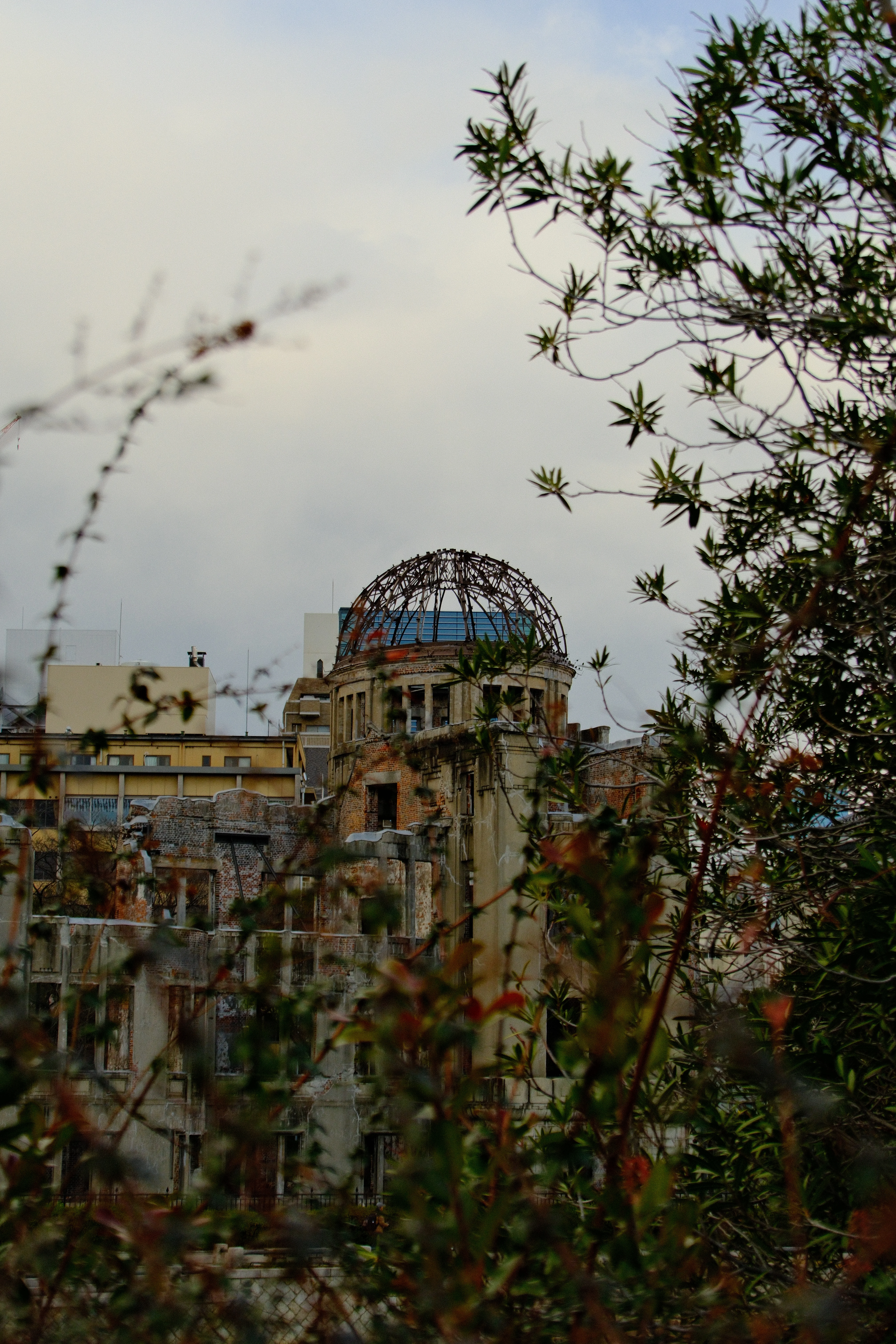 48mm · f/6.3 · 1/1100s · ISO 500
FUJIFILM X-T5 · 16-300mm F3.5-6.7 DC OS | Contemporary 025 · Jan 11, 2026
Ruins of the Hiroshima Peace Memorial behind green foliage.
Hiroshima, Japan
© Brandon Cook